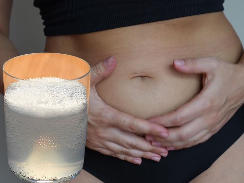 Devojka se drži za stomak, sa leve strane čaša sa soda bikarbonom i vodom