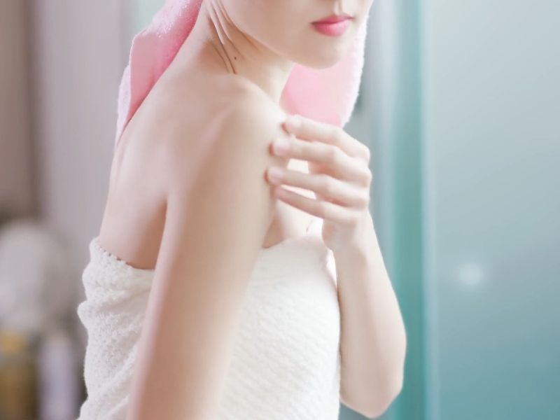 devojka umotana u peškir pregleda svoju kožu