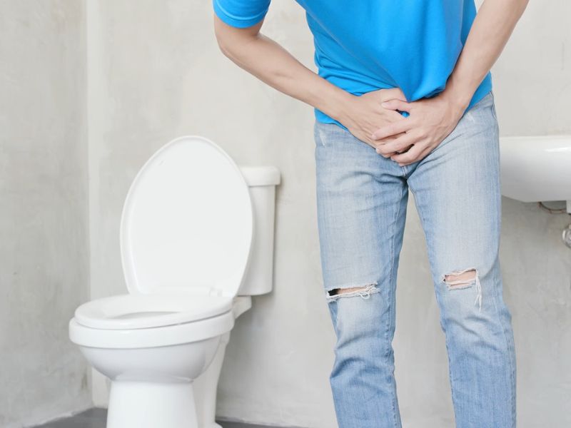 Čovek koji pati od urnarne infekcije se drži za stomak u wc-u
