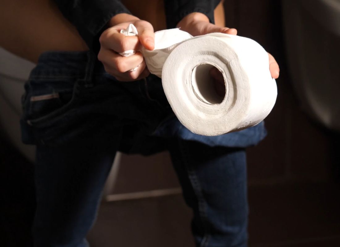 osoba drži toalet papir u ruci i sedi na wc šolji