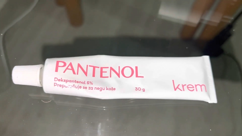Tuba Pantenol kreme sa oznakom 5% dekspantenola položena na staklenoj površini