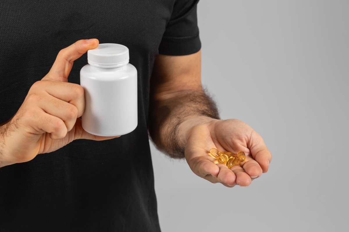 momak u crnoj majici drži kutiju sa suplementima u jednoj ruci i na dlanu u drugoj ruci drži dva suplementa