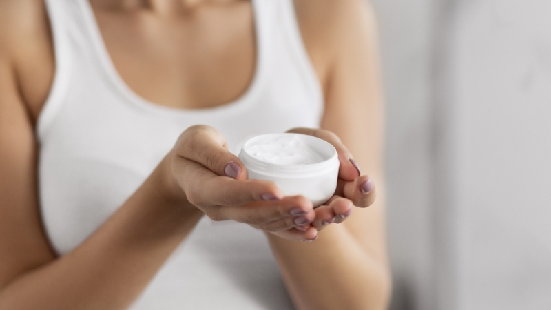 Osoba drži otvorenu teglicu Pantenol kreme u rukama spremnu za nanošenje na kožu