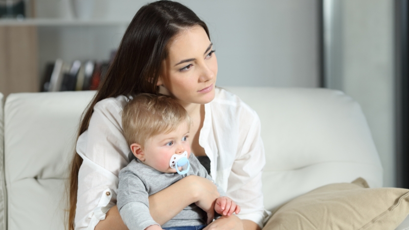Majka drži bebu u naručju i zamišljeno gleda u daljinu