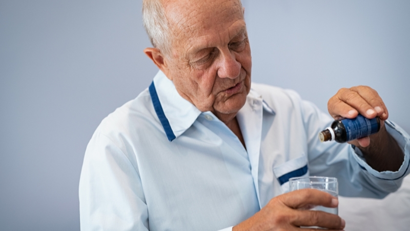 Stariji muškarac uzima melatonin iz bočice i sipa ga u čašu vode