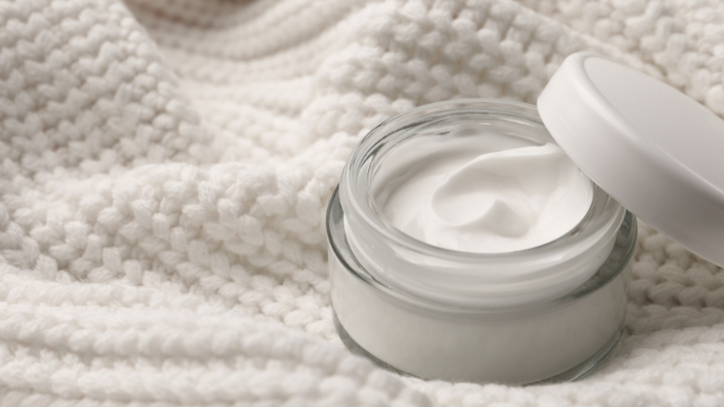 Otvorena tegla Pantenol kreme sa glatkom teksturom postavljena na meku belu tkaninu