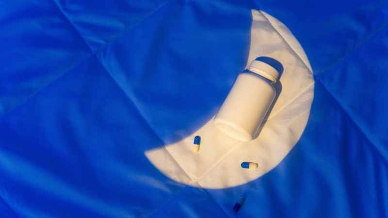 Bočica i kapsule melatonina postavljene na podlozi u obliku meseca pod plavim svetlom