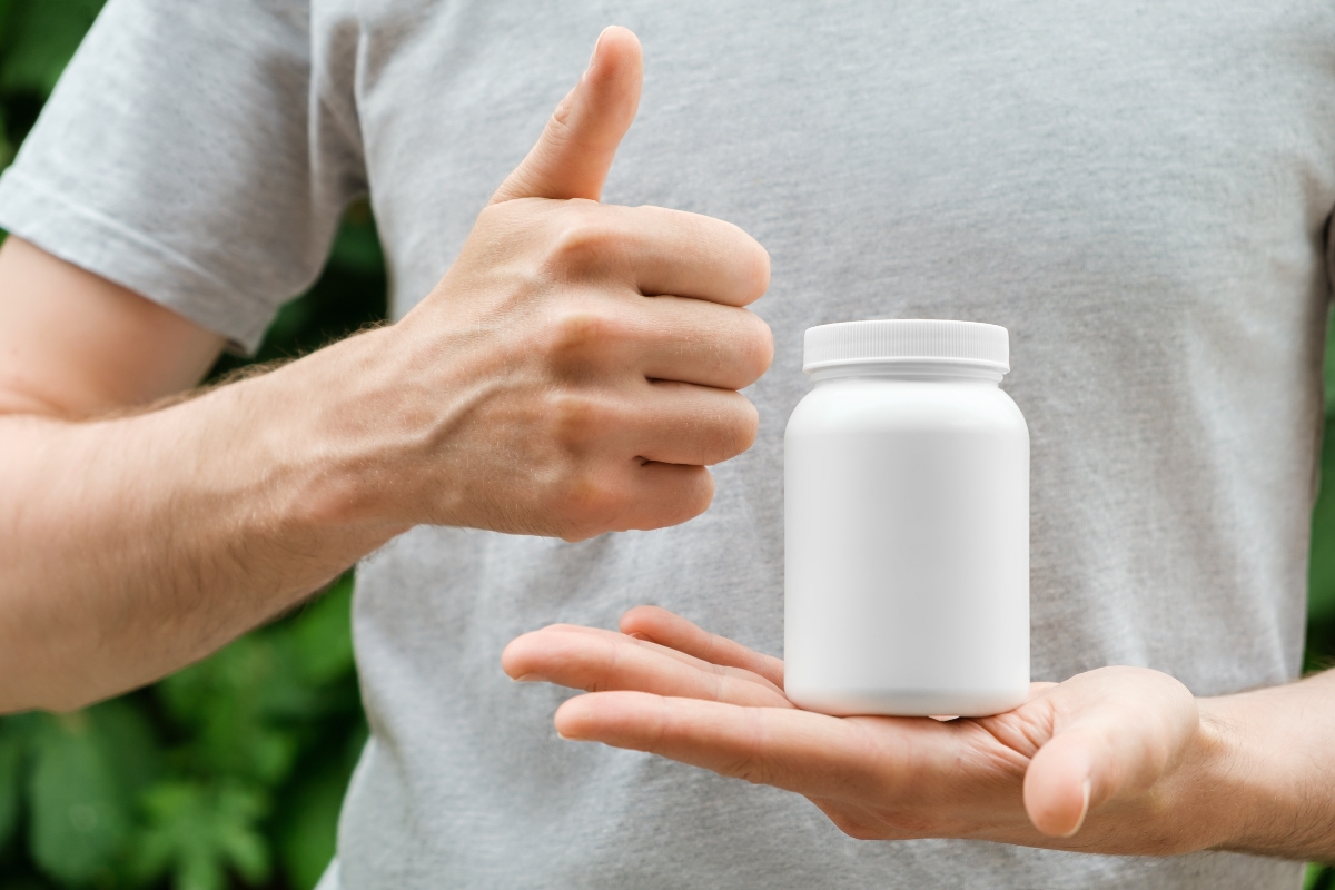 momak drži kutiju sa suplementima na dlanu i podignut palac u obliku lajka