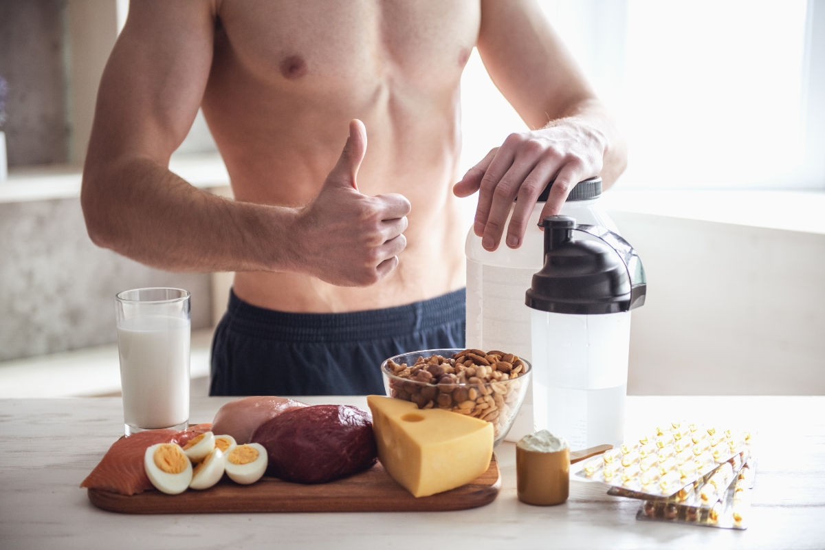 prikaz istreniranog momka bez majice i zdrave hrane na stolu, meso, jaja, šejker, orašasti plodovi i suplementi