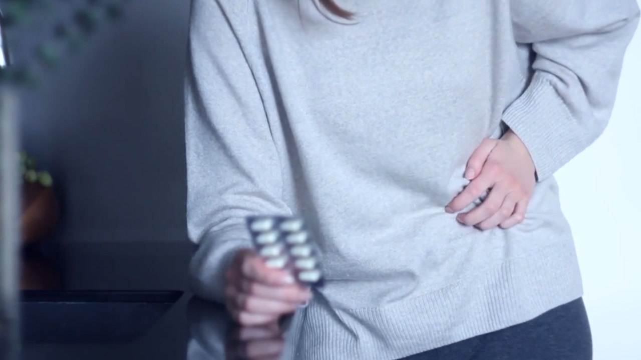 Žena drži blister sa tabletama dok drugom rukom pridržava stomak
