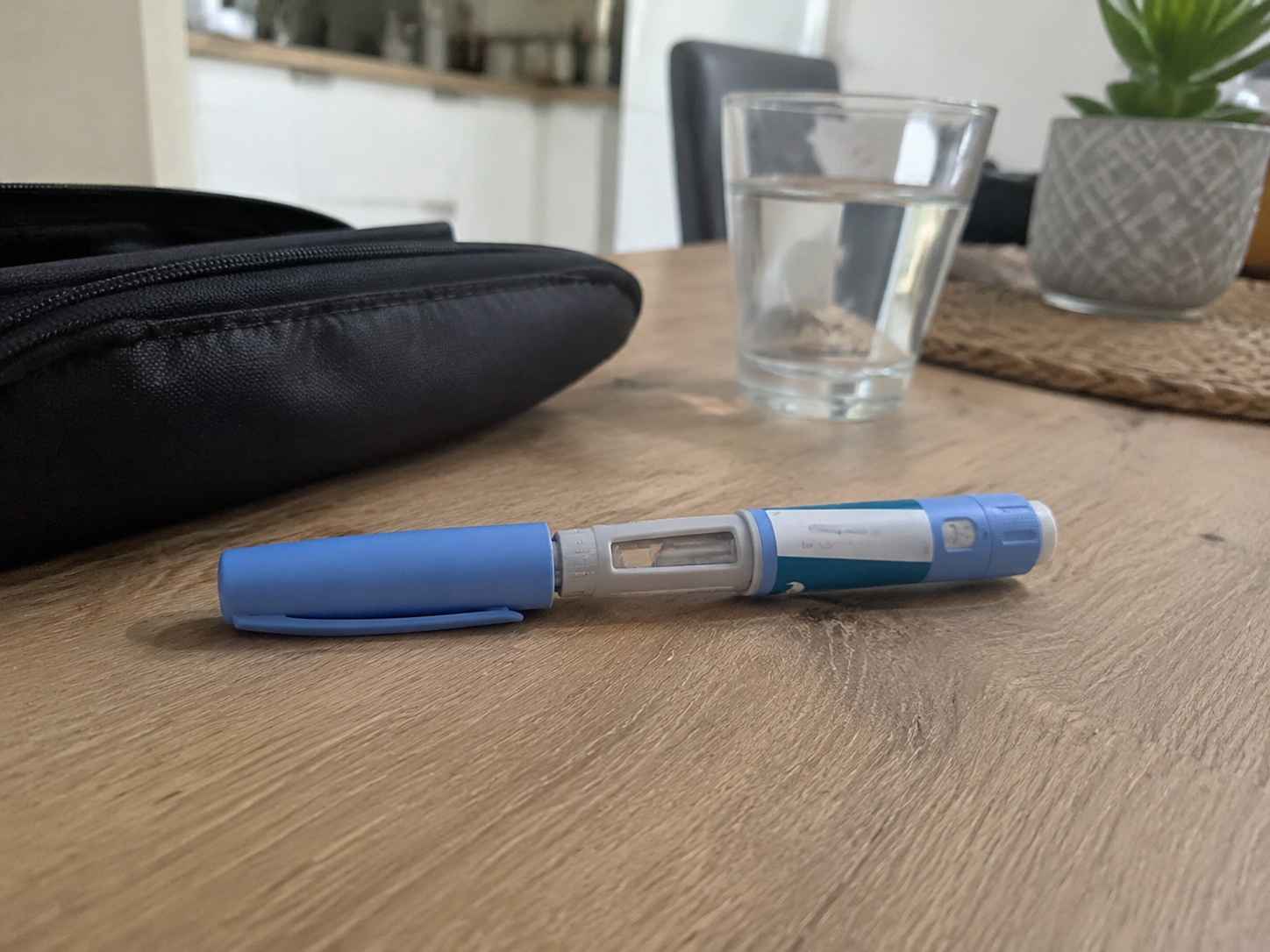 Ozempic pen na drvenom stolu pored čaše vode.