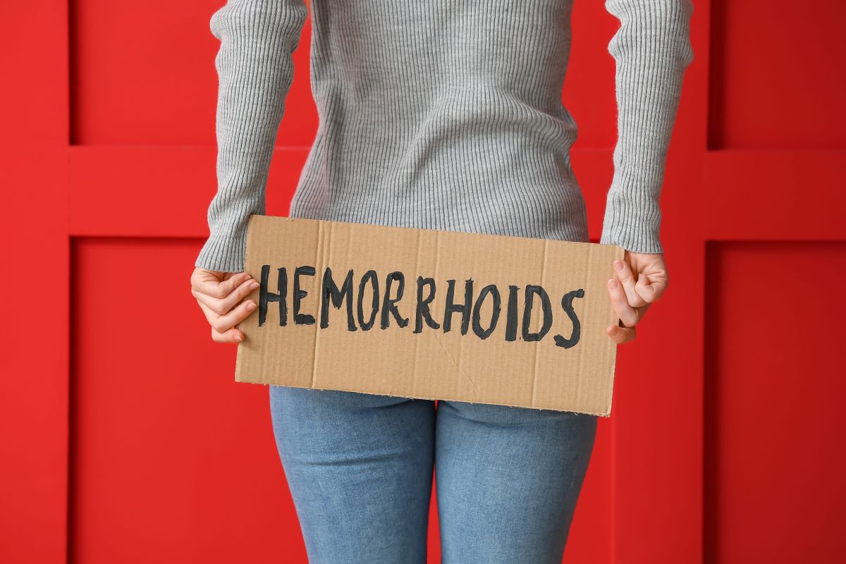 Žena drži kartonski natpis sa rečju „Hemorrhoids“ ispred tela, kao ilustracija teme o tromboziranim hemoroidima